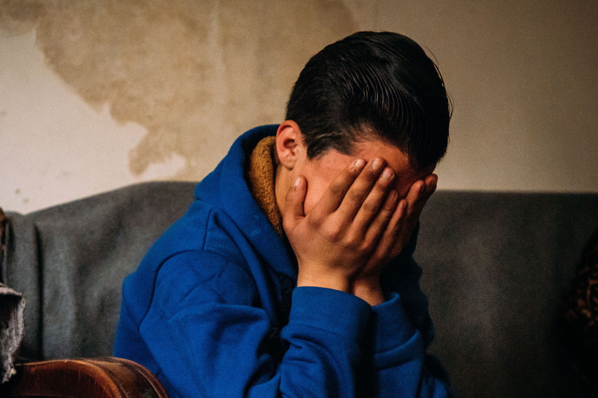 Gutt med kort, mørkt hår og blå genser sitter i en sofa og holder hendene foran ansiktet. SOS-barnebyer jobber for barns rettigheter over hele verden. Foto: Alea Horst