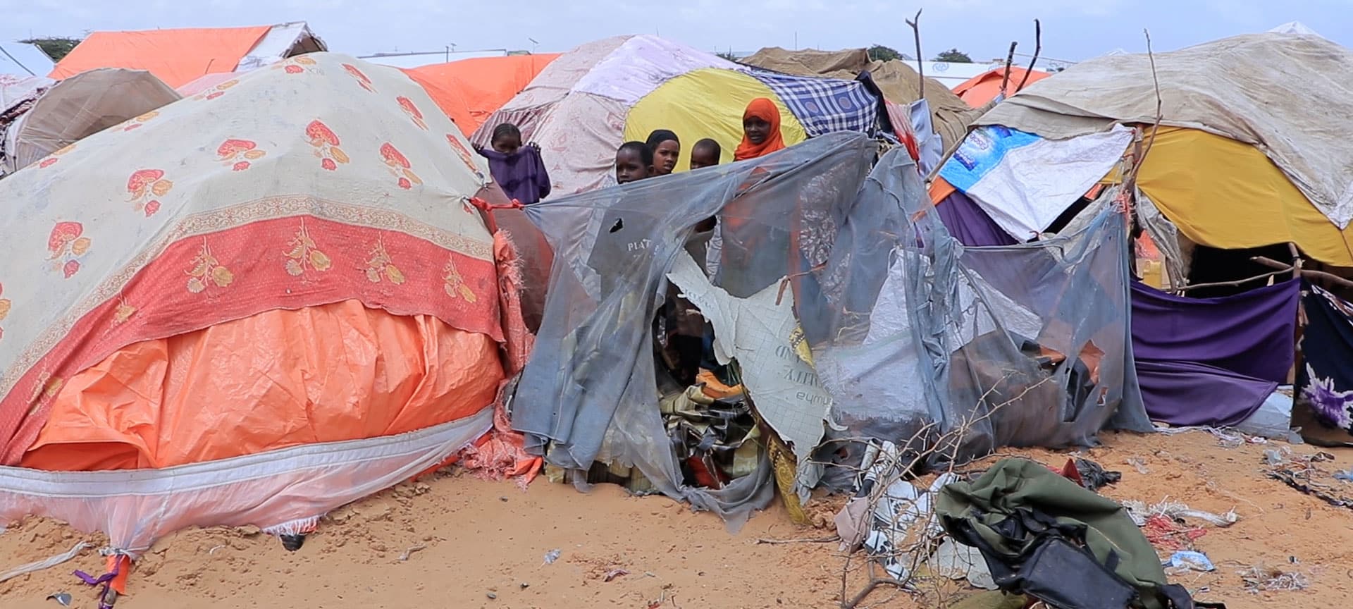 Telt i en flyktningleir dekket av tepper. Flere barn står innimellom teltene. Fra SOS-barnebyers nødhjelpsarbeid i Somalia. Foto: Sunshine Media