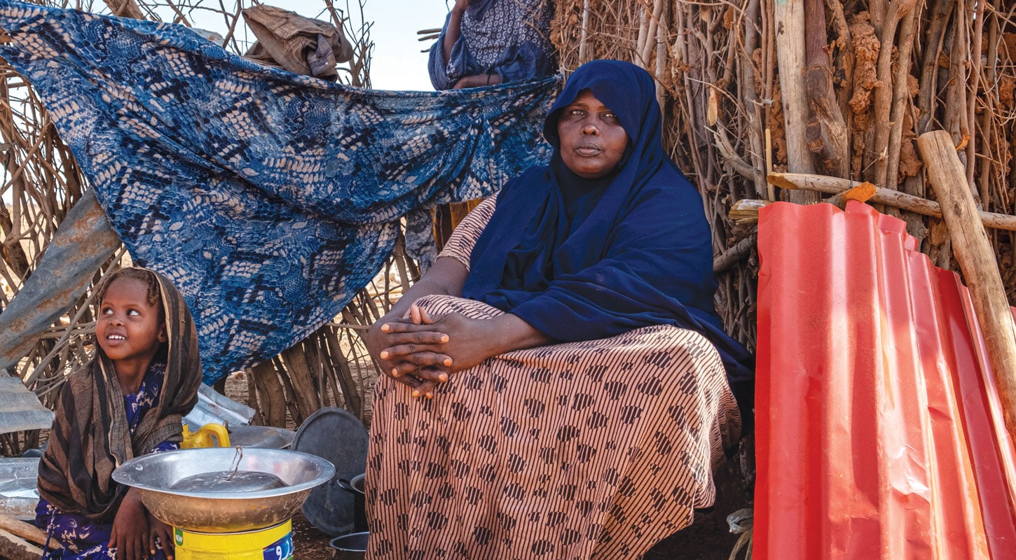 To kvinner fra Etiopia, begge med hijab, sitter foran ei hytte laget av kvister, ei lita jente sitter på bakken . Det er veldig tørt. Foto: Joost Bastmeijer