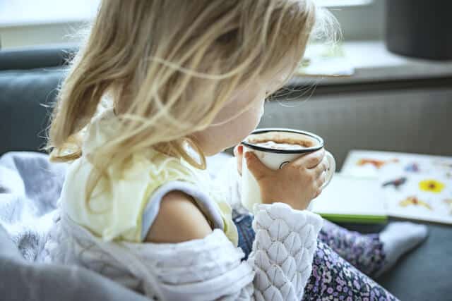 Liten jente i havit genser koser seg i sofaen og drikker kakao. Foto Gerhard Berger