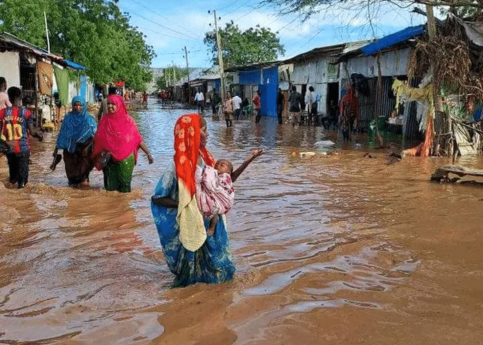 Afrikas Horn: Området rundt husene er oversvømmet av vann. En kvinne bærer et lite barn gjennom vannmassene. Foto: Abdulahi Tarmidi