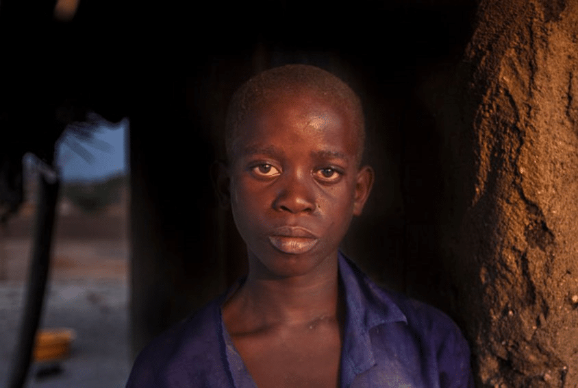 Gutt fra Malawi med et alvorlig uttrykk i ansiktet står lent inntil en vegg laget av leire. Foto: George Kurian