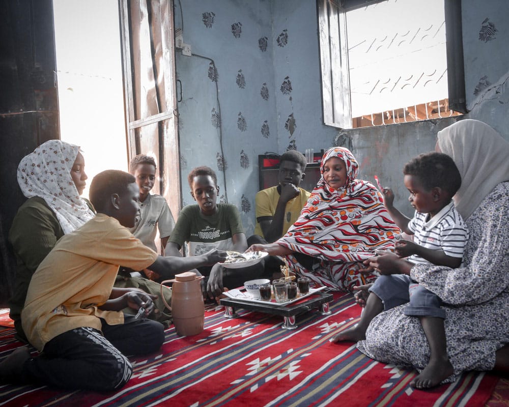 Sudan: Malik sitter sammen med SOS-fosterfamilien sin på gulvet og spiser. Foto: Ali Abdallah Al