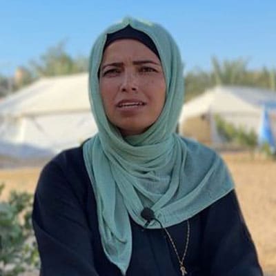 Reem Alreqeb, midlertidig programansvarlig SOS-barnebyer Gaza. hun står foran noen telt og har på seg lys turkis hijab og svart kjole. Foto SOS-barnebyer Palestina