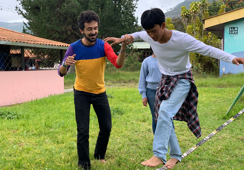 En far med fargerik t-skjorte og svarte bukser støtter sønnen sin som går på ei line. Han har hvit langarmet genser, skjorta knytt rundt livet og jeans. Illustrasjonsfoto til avsnittet Aktivt farskap som handler om å forebygge vold. Eduardo Muriel